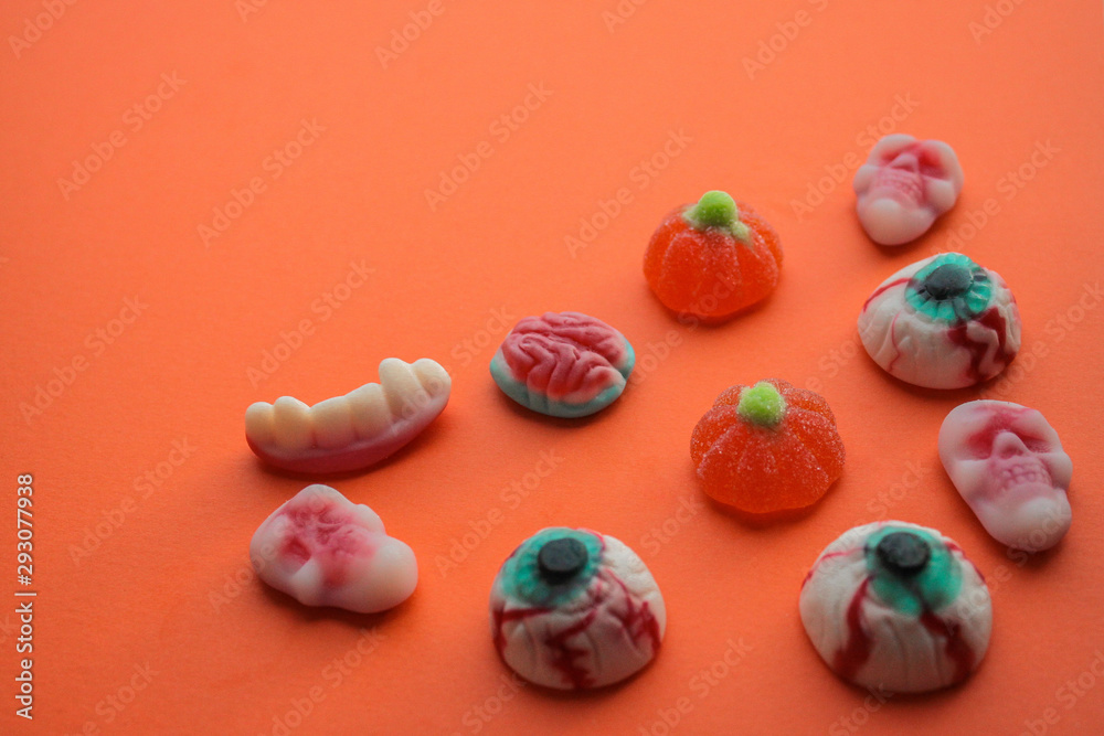 Halloween! Jelly candies in the form of eyes, brains, skulls, teeth with fangs, pumpkins in the lower right corner on a bright orange background. Copy space