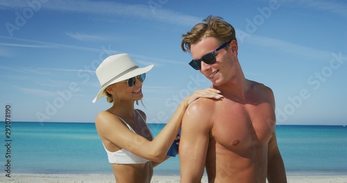 A happy young couple is having fun to apply a sunscreen or sun tanning lotion to take care of their skin during a vacation on a beach.