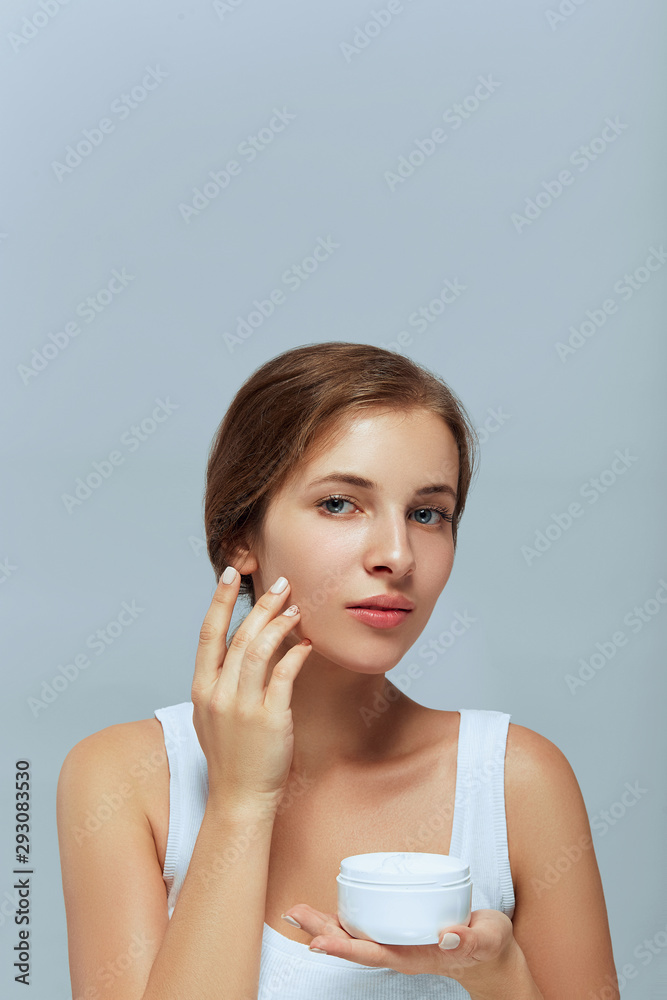 Woman Face Skin Care. Portrait Of Attractive Young Female Applying Cream And Holding Bottle. Closeup Of Smiling Girl With Natural Makeup And Fresh Skin. Beauty Cosmetics. Woman Face Skin Care. Portrait Of Attractive Young Female Applying Cream And Holding Bottle. Closeup Of Smiling Girl With Natural Makeup And Fresh Skin. Beauty Cosmetics.