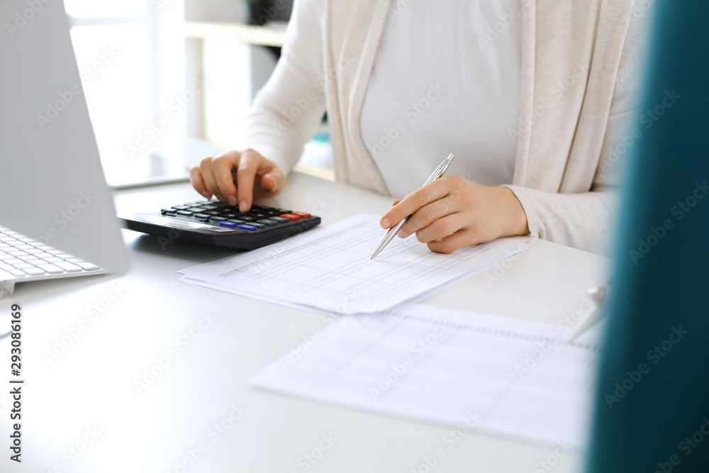 Accountant checking financial statement or counting by calculator income for tax form, hands close-up. Business woman sitting and working with colleague at the desk in office. Audit concept Accountant checking financial statement or counting by calculator income for tax form, hands close-up. Business woman sitting and working with colleague at the desk in office. Audit concept