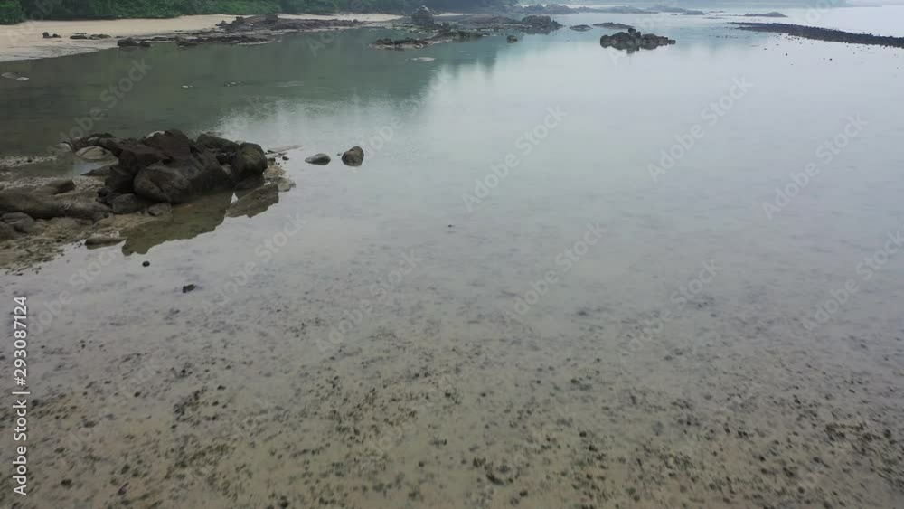 Aerial video. Drone flying low over rocky beach with reflections of mountains and trees.