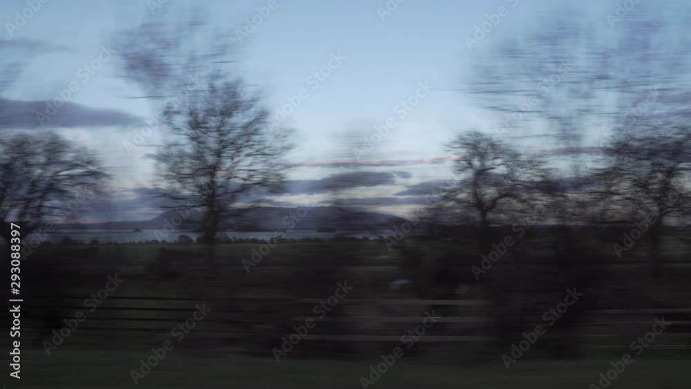 Static shot from vehicle with trees passing by and mountains and lake in the background in wonderful sunset light with nice clouds in Scotland Static shot from vehicle with trees passing by and mountains and lake in the background in wonderful sunset light with nice clouds in Scotland
