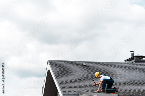 Obraz na plátně repairman in helmet holding hammer while repairing roof
