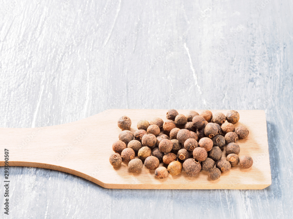 Allspice (Jamaica pepper) on wooden spatula on grey cement background Allspice (Jamaica pepper) on wooden spatula on grey cement background