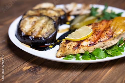 Delicious grilled chicken fillet and eggplant on a plate. Dark wooden table as a background