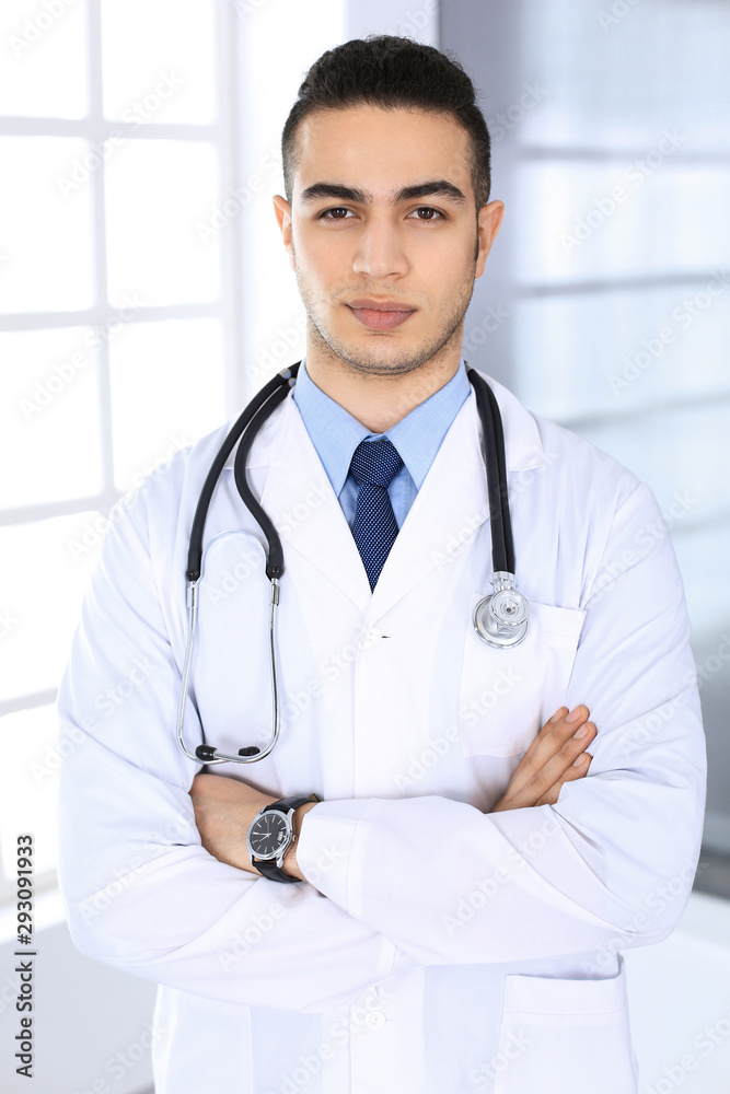Arab doctor man standing with crossed arms in medical office or clinic. Medicine and healthcare concept