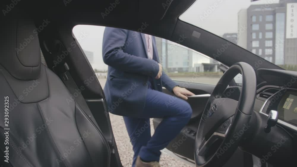 Young man in suit gets in cabin of expensive electric car and starts driving