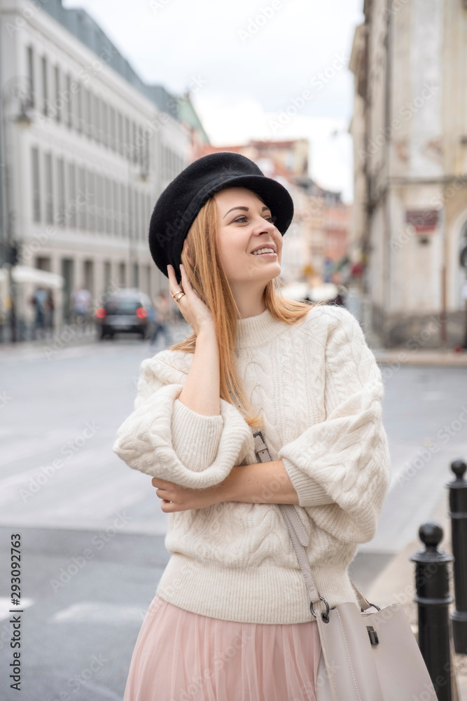 Fototapeta premium Cute cheerful caucasian woman walking on european street. She wear stylish outfit.