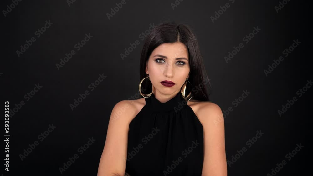 young brunette girl looking at the camera with a displeased face on a black background young brunette girl looking at the camera with a displeased face on a black background