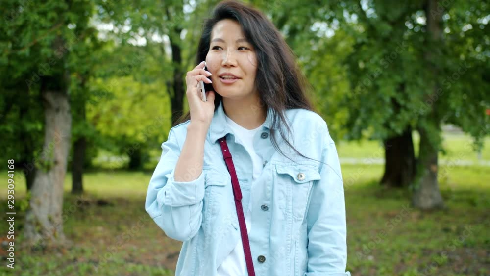 Happy Asian woman student is talking on mobile phone smiling outdoors in city park enjoying modern communication. People, conversation and nature concept. Happy Asian woman student is talking on mobile phone smiling outdoors in city park enjoying modern communication. People, conversation and nature concept.