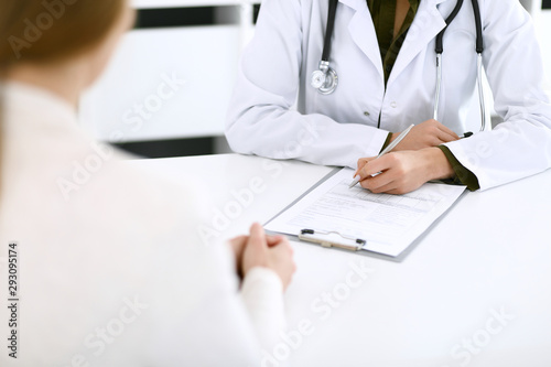 Woman doctor and patient sitting and talking at medical examination at hospital office  close-up. Therapist filling up medication history records. Medicine and healthcare concept