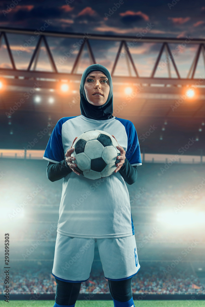 Female muslim soccer player in hijab standing with a ball on a