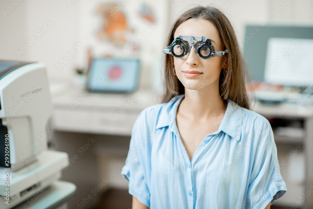 Fototapeta premium Young woman checking vision with eye test glasses during a medical examination at the ophthalmological office