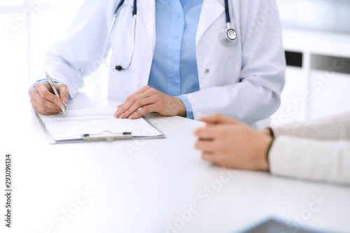 Woman doctor and patient sitting and talking at medical examination at hospital office  close-up. Physician filling up medication history records. Medicine and healthcare concept