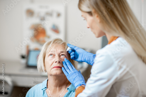 Obraz na płótnie Female doctor dripping eye drops on eyes of a senior patient during a treatment