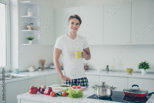 Portrait of his he nice attractive cute cheerful cheery confident guy drinking green tea making dinner lunch at light white modern style interior hotel indoors