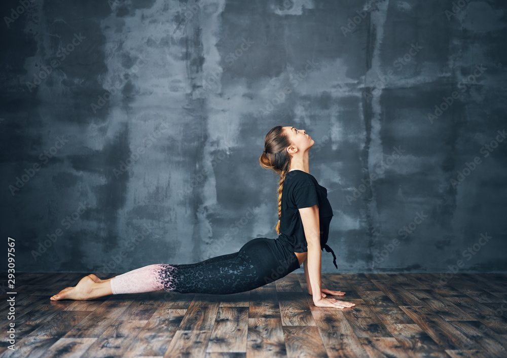 Fototapeta premium Young woman practicing yoga, doing cobra Pose on dark background