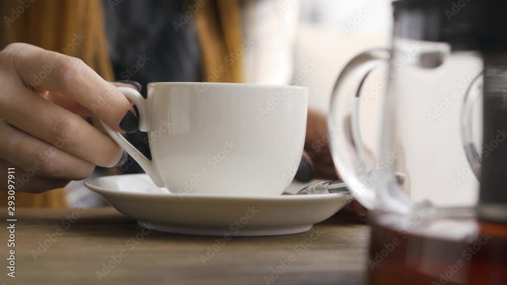 Close-up hand of caucasian woman with black nails touching white tea cup while sitting in cafe. Young woman relaxing indoors. Autumn leisure Close-up hand of caucasian woman with black nails touching white tea cup while sitting in cafe. Young woman relaxing indoors. Autumn leisure
