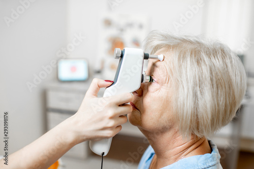 Doctor measuring the eye pressure with modern tonometer to a senior patient in the medical office, close-up photo
