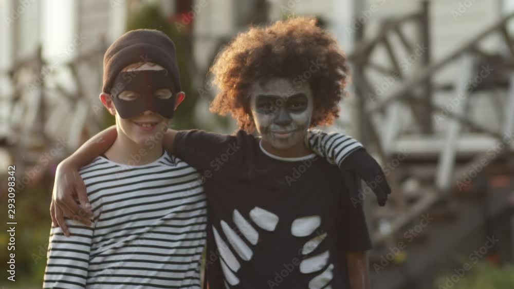 Portrait of two diverse boys wearing Halloween costumes standing together, looking at camera and smiling Portrait of two diverse boys wearing Halloween costumes standing together, looking at camera and smiling
