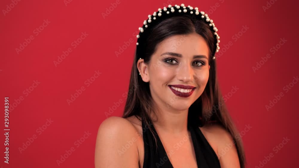 young girl with bright holiday make-up smiling at the camera in the studio. Red background, close-up young girl with bright holiday make-up smiling at the camera in the studio. Red background, close-up
