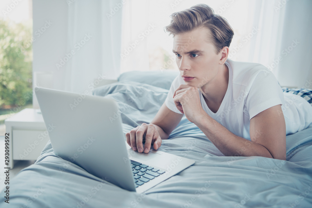 Close up photo of focused pensive blonde haired guy entrepreneur have weekends work use his laptop to make report boss wants lying on bed in house indoors Close up photo of focused pensive blonde haired guy entrepreneur have weekends work use his laptop to make report boss wants lying on bed in house indoors