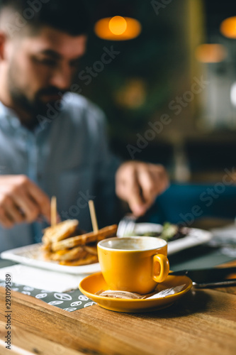 close up of cup of coffee in restaurant. man eating in blurred background