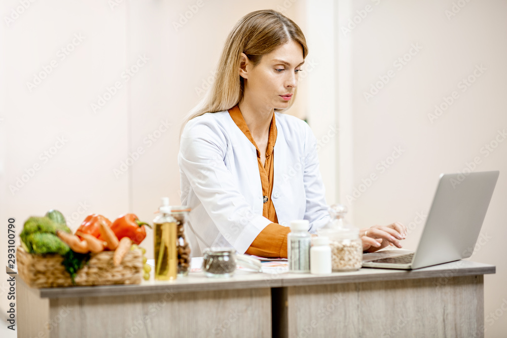Portrait of a confident nutritionist making a diet plan, working at the table with products and a computer in the medical office