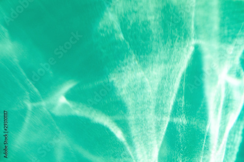 Trendy mint colored abstract background with light and shadows caustic effect. Light passes through a glass. © Aleksandra Konoplya