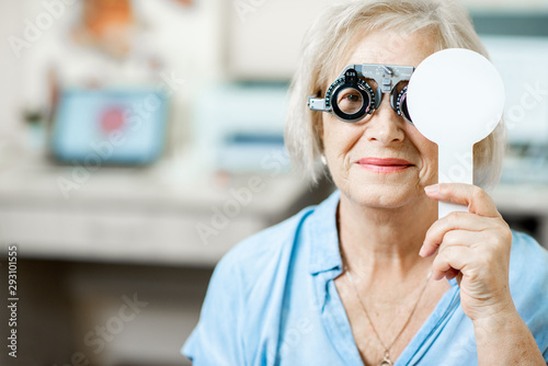 Senior woman checking vision with eye test glasses and scapula during a medical examination at the ophthalmological office