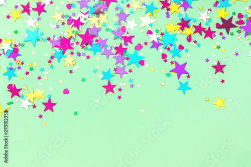 Colorful foil stars confetti sparse on trendy mint colored background. Simple holiday concept. Design template. Frame with copy space for text. Top view, flat lay