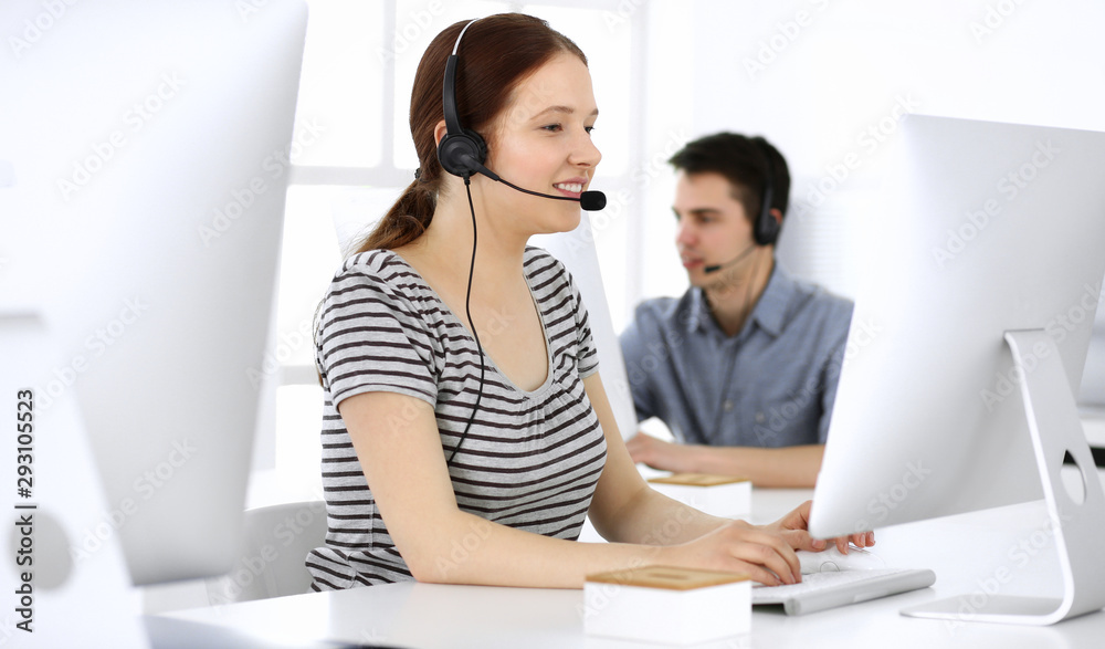 Group of operators at work. Call center. Focus on beautiful woman receptionist in headset at customer service. Business concept and casual striped clothing style Group of operators at work. Call center. Focus on beautiful woman receptionist in headset at customer service. Business concept and casual striped clothing style