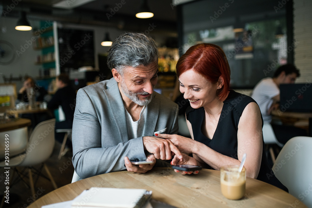 Man and woman having business meeting in a cafe, using smartphone.