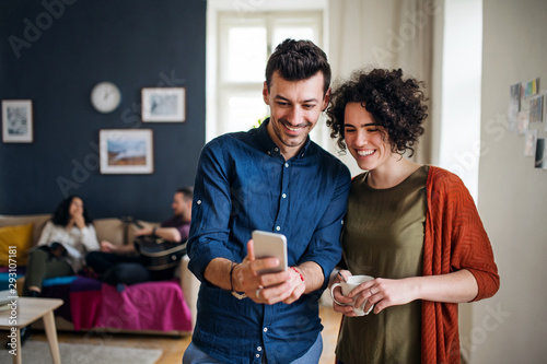 A group of young friends with smartphone indoors, house sharing concept.
