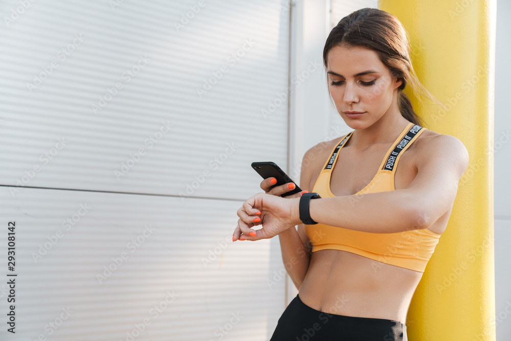 Image of woman holding cellphone and looking at wristwatch outdoors Image of woman holding cellphone and looking at wristwatch outdoors