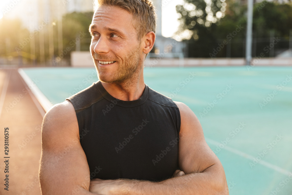 Image of masculine sportsman smiling at stadium outdoors