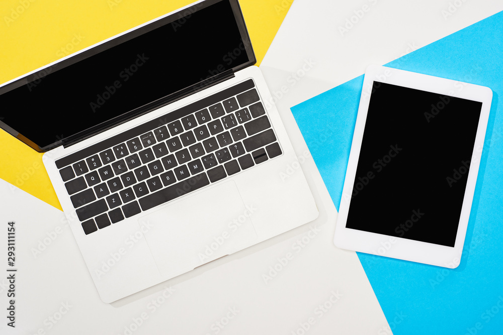 top view of laptop, digital tablet with blank screen on yellow, blue and white background top view of laptop, digital tablet with blank screen on yellow, blue and white background