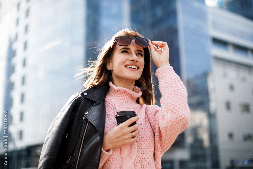 custom made wallpaper toronto digitalPortrait of caucasian woman 20s wearing leather jacket and pink knitted sweater and sunglases drinking takeaway coffee while walking through city street