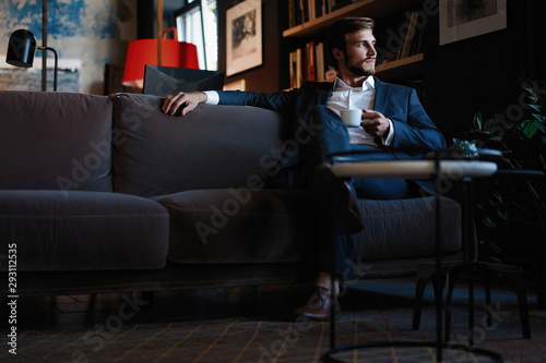 Handsome young man holding coffee cup sitting on the couch in office