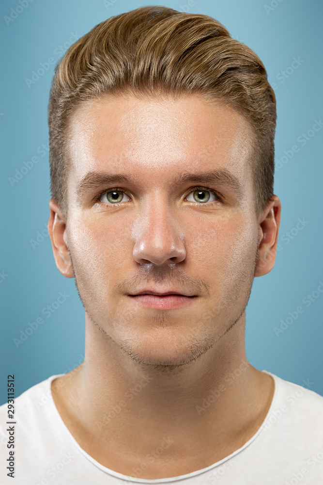 Fototapeta premium Caucasian young man's close up portrait on blue studio background. Beautiful male model with well-kept skin. Concept of human emotions, facial expression, sales, ad, beauty. Looks calm, looking up.