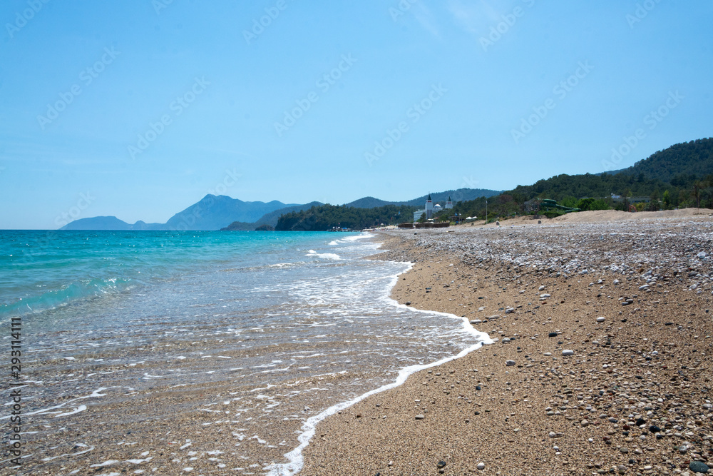 Turquoise sea, slightly rocky beach, mountains in the distance Turquoise sea, slightly rocky beach, mountains in the distance