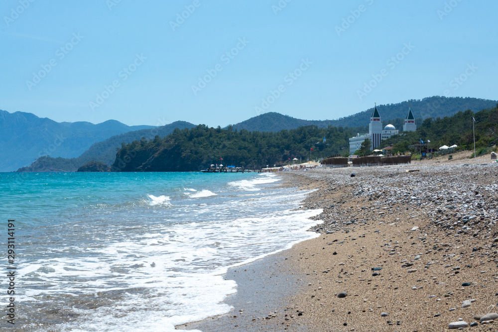 Turquoise sea, slightly rocky beach, mountains in the distance Turquoise sea, slightly rocky beach, mountains in the distance