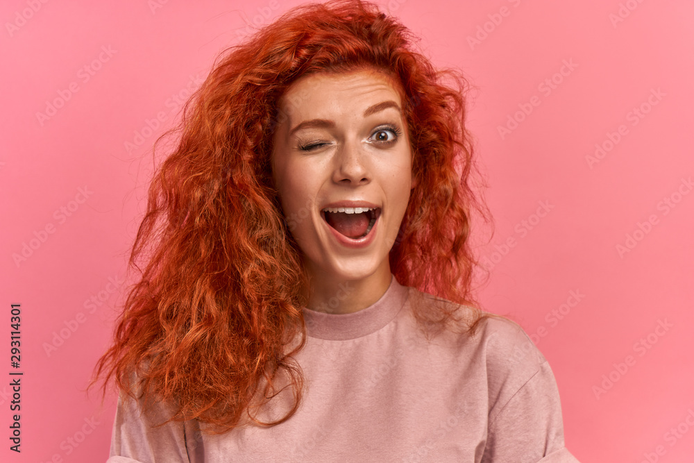 Close up portrait of lovely cute funny redhead lady making winks opening her mouth shouting yeah having holidays dressed in lavender comfortable clothing isolated on pink background