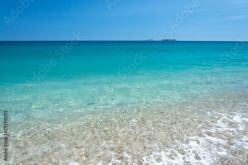 Turquoise sea, slightly rocky beach, mountains in the distance
