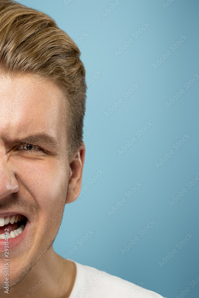 Caucasian young man's close up portrait on blue studio background. Beautiful male model with well-kept skin. Concept of human emotions, facial expression, sales, ad, beauty. Angry screaming. Caucasian young man's close up portrait on blue studio background. Beautiful male model with well-kept skin. Concept of human emotions, facial expression, sales, ad, beauty. Angry screaming.