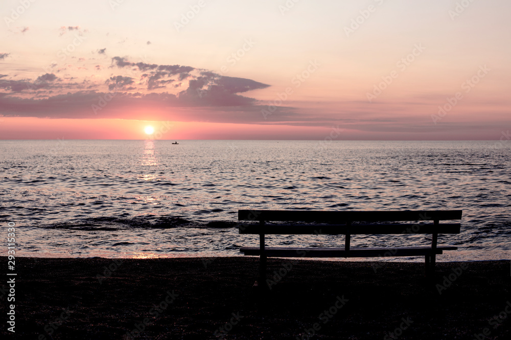 Beautiful sunset (sunrise) over the sea, beautiful waves and outlines of benches on the beach.