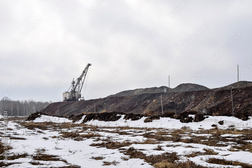 Obraz premium Piles of quartzite with a huge walking excavator and the remains of the forest in the background.