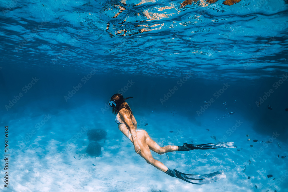 Freediver girl with fins glides over sandy bottom in ocean