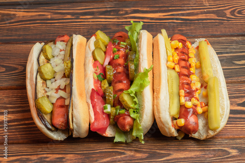 Three hot dogs with Bratwurst sausages on a dark wooden background. Fast food, Business lunch. Street meal. Quick snack