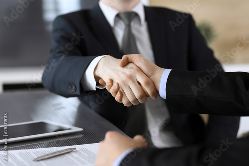 Businessman shaking hands with his colleague or partner above the glass desk in modern office  close-up. Unknown business people at meeting. Teamwork  partnership and handshake concept